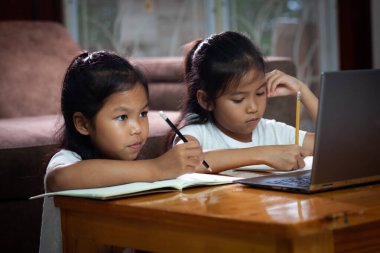 İki Asyalı kız kardeşi ile çevrimiçi teknoloji öğrenmek için dizüstü bilgisayar kullanıyor. Çevrimiçi eğitim kavramı, karantina ve okul tatillerinde evde sosyal mesafe öğrenimi.