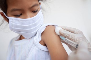 Doktor, Asyalı çocuk koluna aşı yapıyor. Başbakan 2.5 ve Covid-19 virüsleriyle hava kirliliğini korumak için koruyucu maske takan kız çocuğu. Sağlıklı ve tıbbi konsept.
