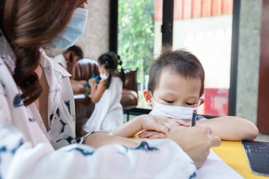 Evden çalışıyorum. Coronavirus COVID-19 karantinaya alınırken anne oğluyla öğretiyor ve oynuyor. Anne ve oğul koronavirüs salgını sırasında evde çalışırken koruyucu maske takıyor..