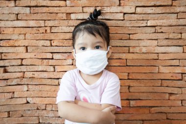 Korunma maskesi takan Asyalı küçük kız Coronavirus Covid-19 'u ve Başbakan 2.5 anti-duman ve virüslerle hava kirliliğini korumak için evde kalıyor. Hava kirliliği ve Tıbbi Konsept.