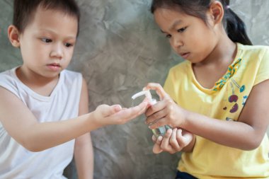 Asyalı çocuk ve kız, virüs ve bakteri bulaşmasını önlemek için dezenfektan jel kullanıyor..