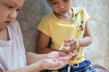 Asyalı çocuk ve kız, virüs ve bakteri bulaşmasını önlemek için dezenfektan jel kullanıyor..