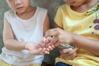 Asyalı çocuk ve kız, virüs ve bakteri bulaşmasını önlemek için dezenfektan jel kullanıyor..