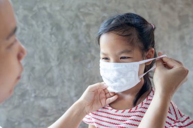 Asyalı anne, Coronavirus Covid-19 salgınını ve 2,5 numaralı hava kirliliğini korumak için kızının koruyucu maske takmasına yardım ediyor.