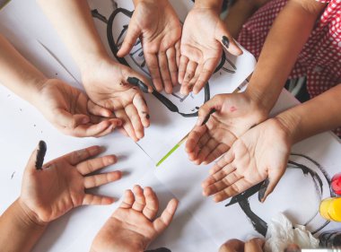 Bir grup çocuk birlikte oynamak için ellerini suluboya resme hazırlıyor.