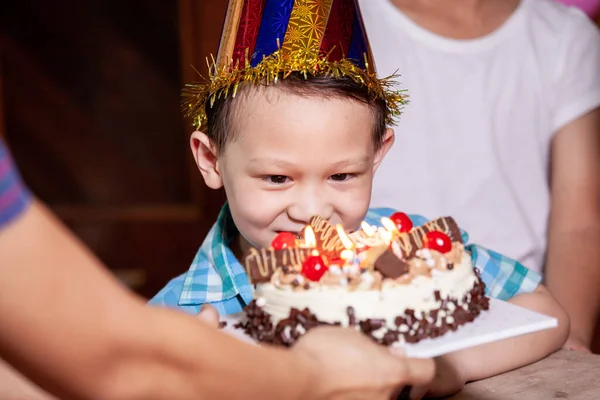 Cute asian child boy is surprising with delicious birthday cake which his mother give to him. Child is blowing candles on birthday cake in the party with fun and happiness.