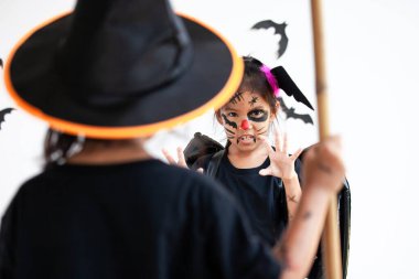 Cadılar Bayramı 'nda cadılar bayramı kostümü ve makyaj giymiş iki tatlı Asyalı kız çocuk birlikte eğleniyorlar.