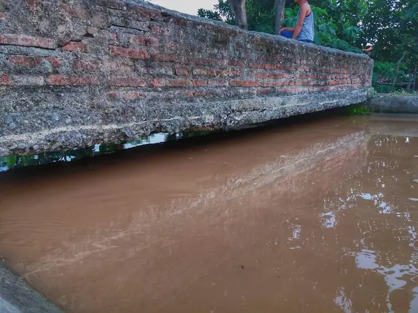 Yaya köprüsü. Yığından ya da tuğladan yapılmış binalar. Kirli nehir köprünün altından akıyor.