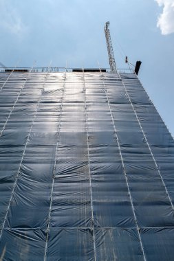 Güneşli bir günde iskele sistemi ve vinçle inşa edilmiş yüksek katlı bir bina.