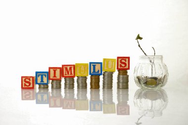Conceptual economic stimulus by government during crisis or Covid-19. Wooden alphabet block on on stacked coins. Coins in mini glass jar with half-dead plant. Focus on wooden alphabet. clipart