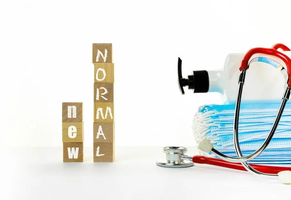 Tahta blokta beyaz yazılar var. Yüz maskeleri, el dezenfektanı, görüş mesafesinde steteskop. Covid-19 yüzünden kavramsal olarak yeni normalleri kucaklamak. Küplere seçici odaklanma.