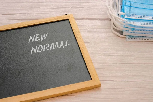 Tahta üzerinde yazı olan yazı tahtası. Tek kullanımlık yüz maskeleri görünür. Yaşam tarzı olarak yeni normal kavramı. Seçici odak.