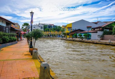 Malacca City, Malezya - 2019 Aralık 19: Yaya geçidi, nehir kenarındaki yenilenmiş binalar ve mavi gökyüzü ile güzel bir Malacca nehri. Nehir yolculuğu rotası. Önplanda seçmeli odak.