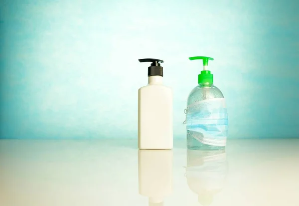 Hand sanitizers side by side where one is covered by face mask over blue background. Conceptual of keeping sanitized hands and wearing face mask. Selective focus.