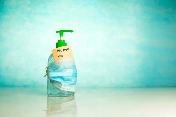 Mavi arka planda mesaj alanı olan yüz maskesi ile kaplı izole edilmiş el dezenfektanı. Ellerini sterilize etme ve yüz maskesi takma kavramı. Seçici odak.