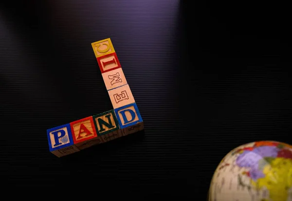 Dünya Sağlık Örgütü tarafından ilan edilen koronavirüs salgını. Gösterişsiz görüntü. Koyu yüzeyde tahta alfabe küpleri ve kısmen görülen dünya. Sadece seçici küplere odaklan.