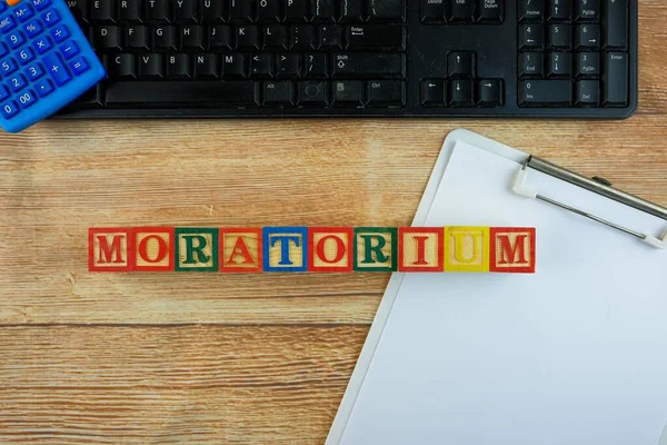 Ekonomik kriz ve durgunluk dönemindeki bankaların moratoryumun kavramsal görüşü. Klavye, hesap makinesi, kalem, beyaz kağıt, alfabe küpleri ahşap masada. Panonun tepesine odaklan.