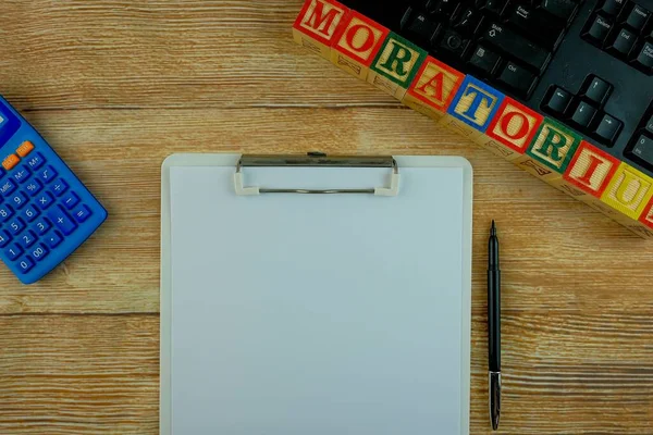 Bankaların finansal kriz ve ekonomik durgunluk sırasındaki geri ödeme erteleme opsiyonunun kavramsal görüşü. Klavye, hesap makinesi, kalem, beyaz kağıt ve alfabe küpleri MoratORIUM üzerine ahşap doku. Sadece seçici küplere odaklan.