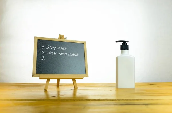 Metinler temiz kalıyor tebeşirde yüz maskesi takılıyor. Koronavirüs salgını sırasında hijyenik kalma kavramı. Tahta masada el dezenfektanı ve karatahta izole edilmiş. Sadece tahtaya odaklan..