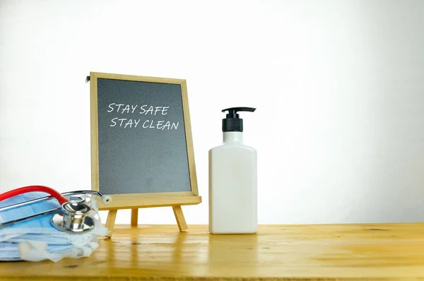 Texts STAY SAFE STAY CLEAN on chalkboard. Conceptual of staying hygienic during coronavirus outbreak. Hand sanitizer and chalkboard isolated on wooden table. Focus on chalkboard only.