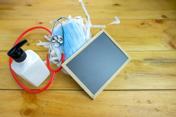 Ölümcül virüs salgını sırasında hijyenik kalma ve sağlık kontrolü alma kavramı. El dezenfektanı, yüz maskeleri karatahta tahtası ve steteskop. Siyah tahtaya odaklan.