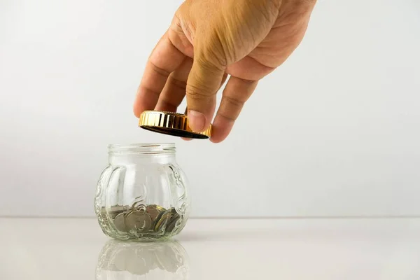 Kilit altındaki kötü zamanlar için kavramsal disiplinli tasarruflar veya Coperid-19 veya finansal kriz. İçinde bozuk para olan cam kavanozun kapağını tutan adamın eli. Yansıtıcı tablo. Dış kavanoza odaklan.