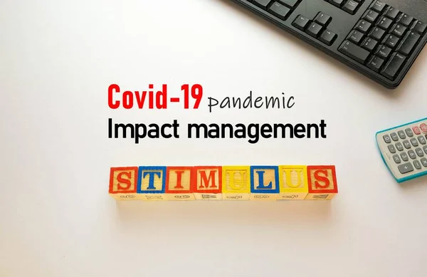 Covid-19 'un beyaz üzerine salgın etkisi yönetimi metni. Kriz veya Covid-19 döneminde etki yönetimi üzerine kavramsal hükümet ekonomik uyaranı. Hesap makinesi klavyesinin üst görünümü ve beyaz harf blokları. Metne seçici odaklanma.