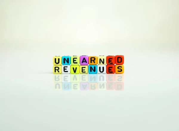 onceptual of unearned revenues in  financial statements. Colorful alphabet beads isolated over reflective white surface. Focus of text R at center. Others in gradient blur.