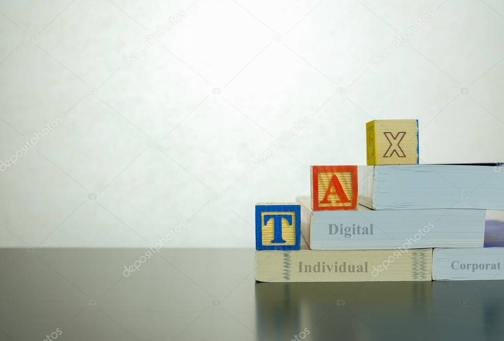 Conceptual image of increasing tax and annual tax return. Stacked wooden block letter forming TAX on stacked books on dark reflective surface. Focus at block letter A.