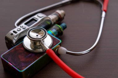 Elektronik sigaraların sağlık güvenliğinin belirsizliğinin kavramsal görüntüsü. Yakından izole edilmiş kırmızı steteskop koyu arkaplandaki buhar kitlerini teşhis ediyor. Çan diyaframına odaklan..