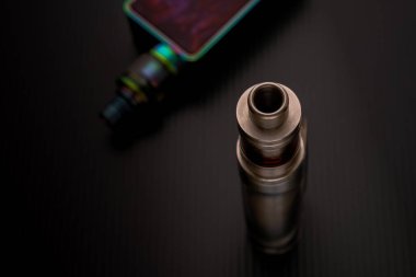 Ağızlığa ve bataryaya koyu yüzeyde bağlı olan atomizörün izole edilmiş yakın çekimi. Son zamanlarda e-sigaranın sağlık güvenliğinin belirsizliği kavramı. Üst görünüm.