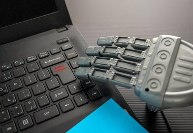 Siyah bir defterin kırmızı metinleriyle tuş takımının yanında robot el. Kulaklık kısmen görünür. Kırmızı metinli tuş takımına odaklan. Yapay zekanın kavramsal görüntüsü (AI).