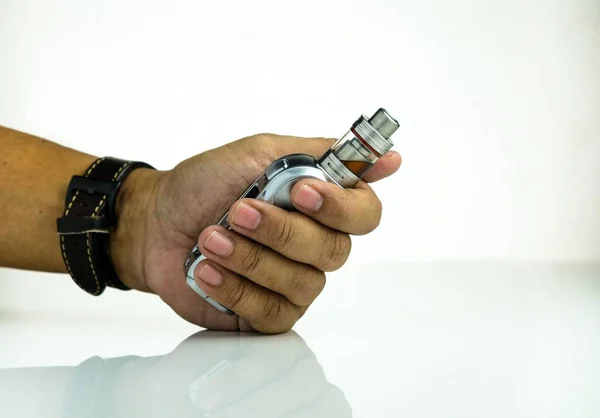 Adamın sol eli, ağızlık ve bataryayı yansıtıcı beyazın üzerine yapıştırılmış atomizer ile buharlaştırma kiti tutuyor. Son zamanlarda e-sigaranın sağlık güvenliğinin belirsizliği kavramı. Etiketlere odaklan.