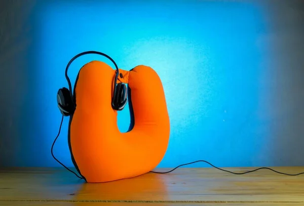 Tatil sezonunun kavramsal görüntüsü. Kulaklıklar ahşap yüzeydeki turuncu boyun yastığına bağlı. Mavi arka plan. Kulaklığa odaklan. Diğer gradyan bulanıklığı.