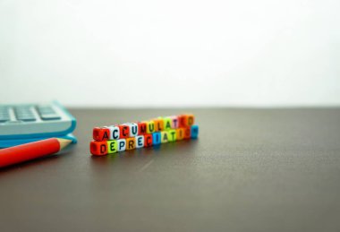 Finansal beyanlarda birikmiş değer kaybı kavramı. Karanlık masanın üzerinde renkli alfabe boncukları kelimeleri oluşturuyor. Kalem ve hesap makinesinin yanı sıra ön taraftaki boncuklara odaklan.