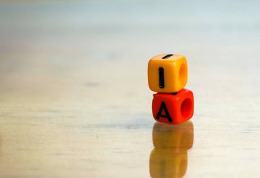 Gelecekteki bilişim teknolojilerinde yapay zeka kavramı. Yansıtıcı yüzeyde birbirinden izole edilmiş iki renkli alfabe boncuğu. Boncuklara odaklan. Diğer gradyan bulanıklığı.