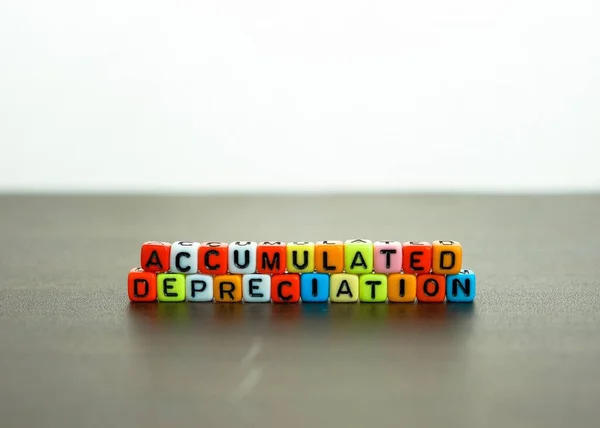 Finansal beyanlarda birikmiş değer kaybı kavramı. Renkli alfabe boncukları kara masanın üzerine dizilmiş kelimeleri oluşturuyor. Spiral defter ve kalem görünür. Öndeki boncuklara odaklan.