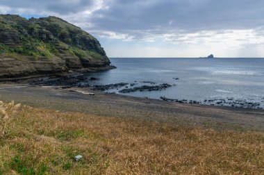 Jeju Güney Kore 'nin Yongmoeri Hyean adlı güzel kayalık sahil manzarası. Sanbangsan okyanusa doğru uzanıyor. Akşamüstü güneşli, alçak gelgit sırasında.