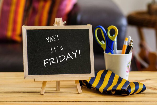 Image of yay it's Friday on chalkboard. Besides stationery in mug. Selective focus on notice board. Others in gradient blur.
