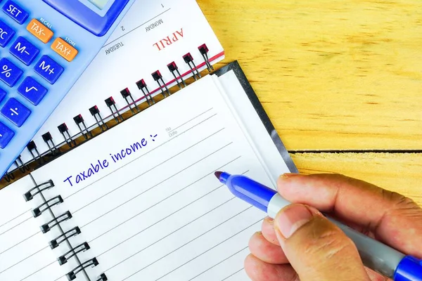 Nisan ayında vergi iadesinin kavramsal görüntüsü. Boş not defterine kalem yazan parmaklar. Hesap makinesi görünür. Boncuklara odaklan. Ahşap arkaplan.