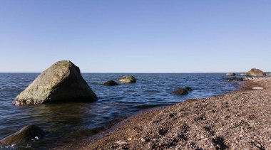 Manzara: Sahilde granit çakıl taşları ve denizde granit kayalar.