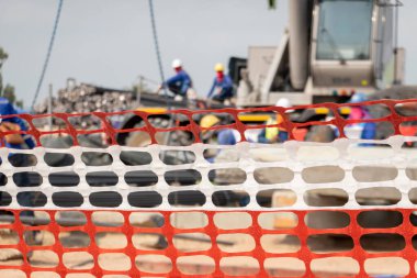 İnşaat alanında arka planda kasklı işçiler var..