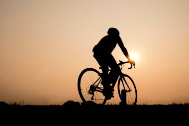 Bisikletli adam bisiklete biniyor. Bisiklet sporu sporu sporu sporcusu gün batımına doğru açık bir yolda bisiklet sürüyor.
