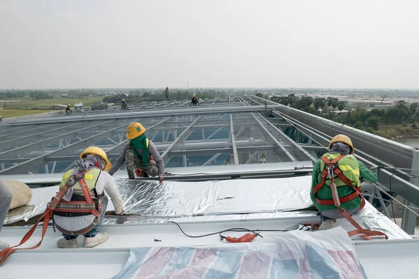 Construction worker wearing safety harness and safety line working on a metal industry roof new warehouse