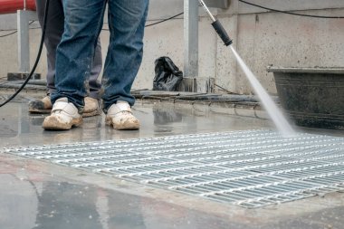 İnşaat işçisi beton zemini yüksek basınçlı su jetiyle temizliyor.