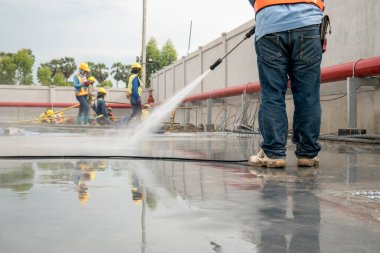 İnşaat işçisi beton zemini yüksek basınçlı su jetiyle temizliyor.