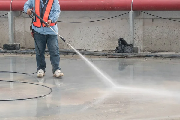 İnşaat işçisi beton zemini yüksek basınçlı su jetiyle temizliyor.