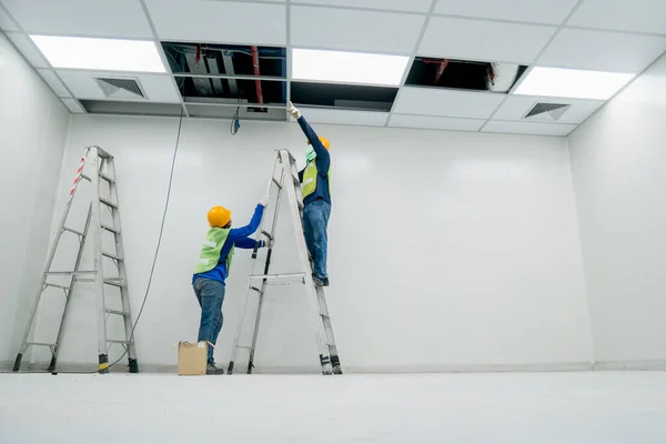 Güvenlik üniformalı elektrikçi beyaz odada çalışıyor.