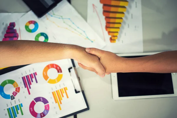 Men shaking hands. Top view of two men shaking hands and business report background