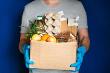 Çevrimiçi alışveriş kavramı. Erkek kurye, Coronavirus karantinası sırasında eve taze yiyecek getiren bir market kutusuyla koruyucu eldivenler, yakın plan..